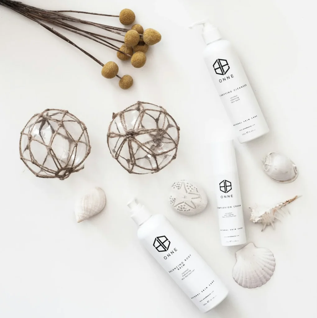 White skincare bottles arranged with shells and dried botanical stems